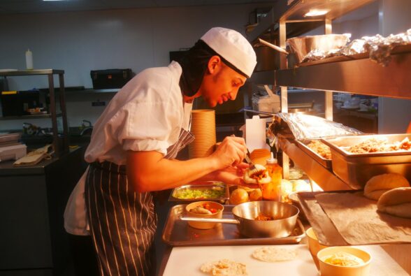 Isaiah Connor, a Professional Culinary Arts Level 2 student, prepares pulled pork bao buns, served with pickled shallots, chilli and coriander for a customer in The Kitchen.