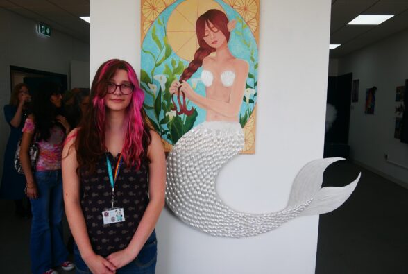 Quin Gundry, Creative Practice Art, Design and Communications Level 3 Extended Diploma, standing by her Mermaid mixed media picture.