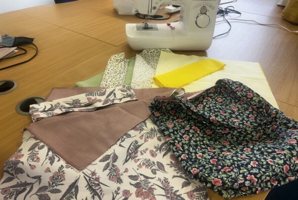pieces of floral material cut out as tote bag pattern pieces on a table in front of a sewing machine